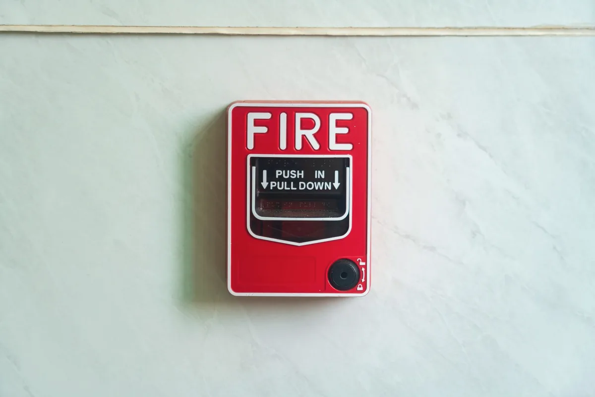 Red manual fire alarm pull station on a pale textured wall