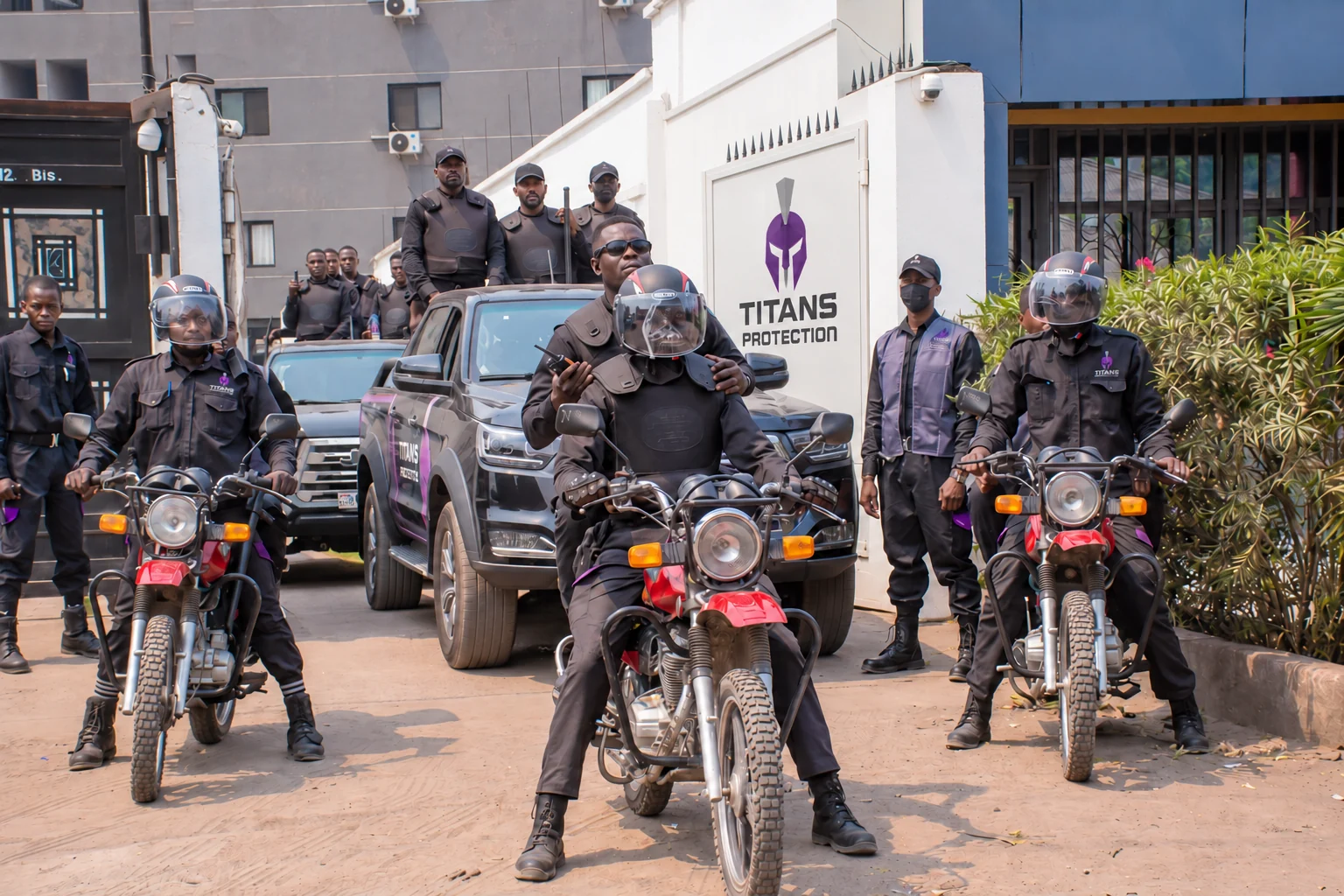 Titans motorcycle officers and vehicle team outside the company entrance, with a restored white gate and enlarged Titans Protection logo